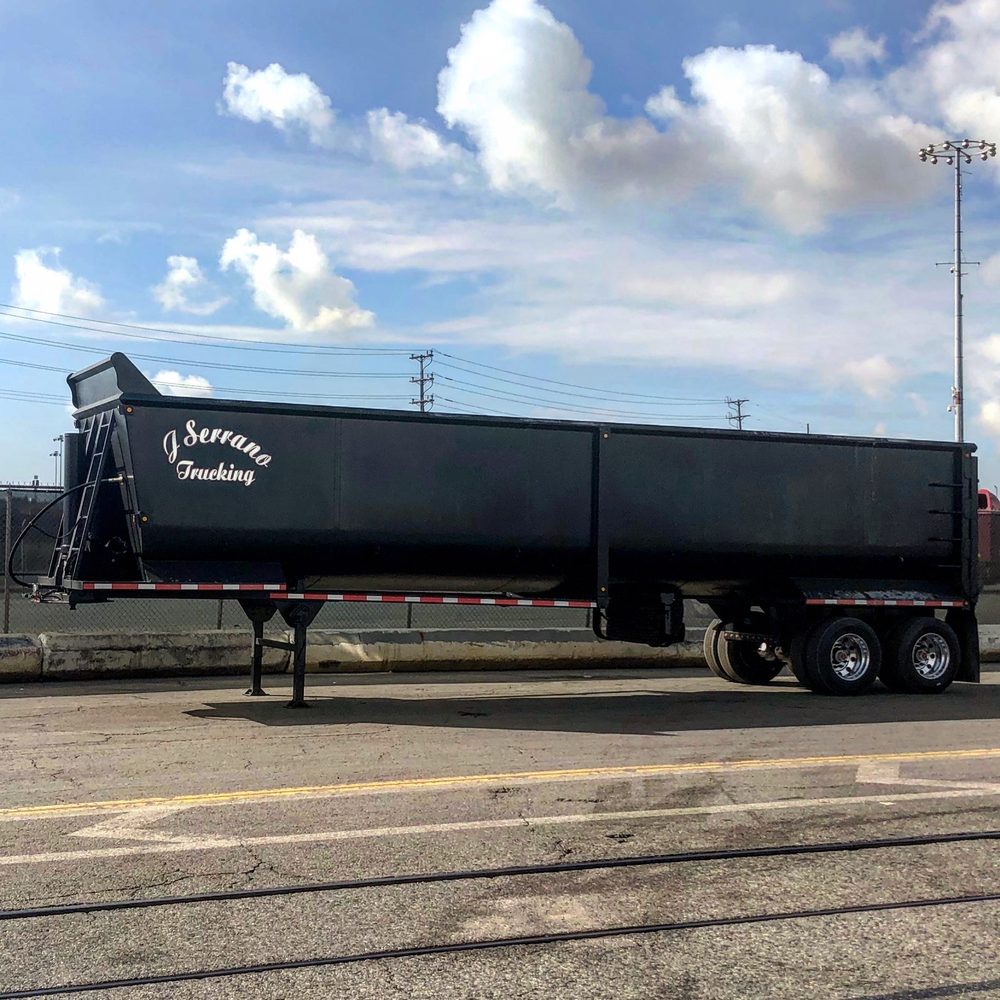 Black end dump trailer seen from the side, coupled to a tractor