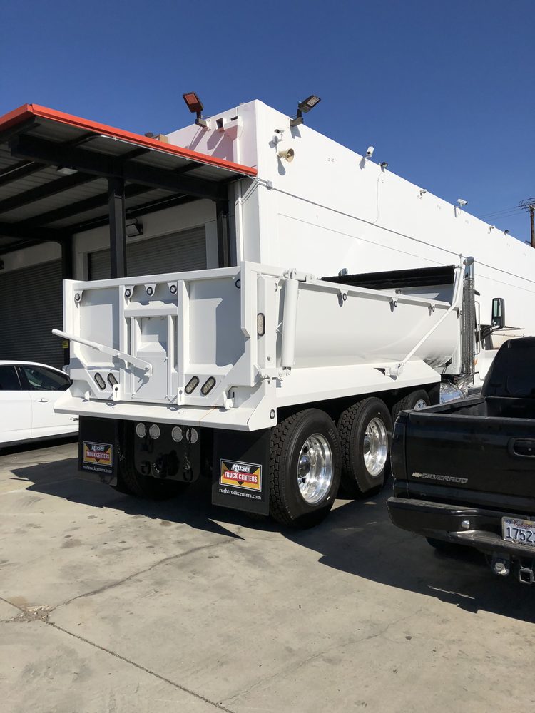 White dump body sitting on its chassis under a shop canopy