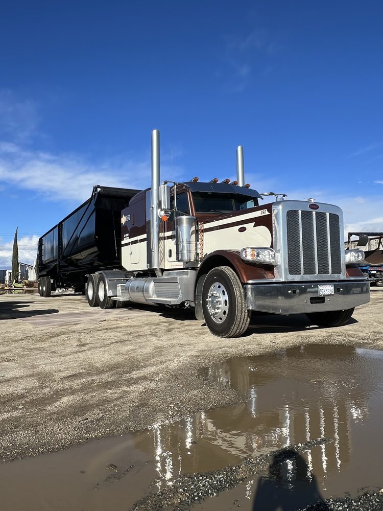 Cream and brown Peterbilt with a black dump body, standing water reflecting it