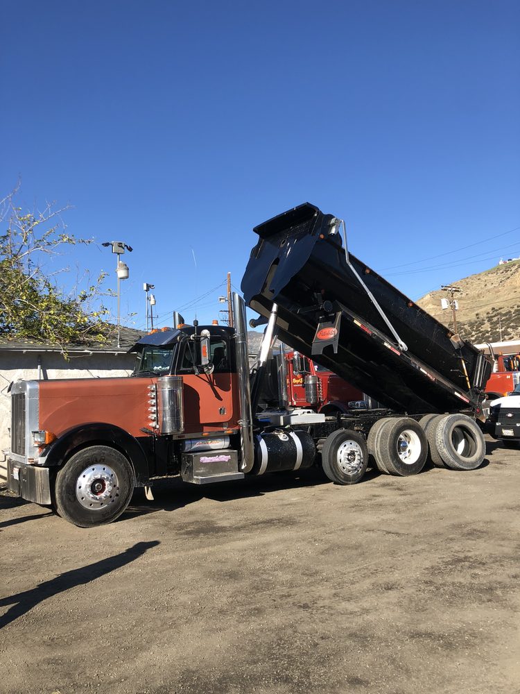 Black dump body raised on an orange truck