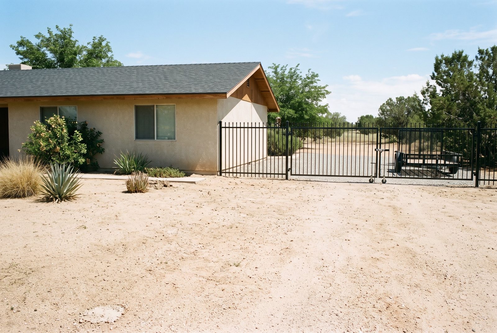 Design rendering of a black steel picket fence and wide trailer gate beside a single story desert home