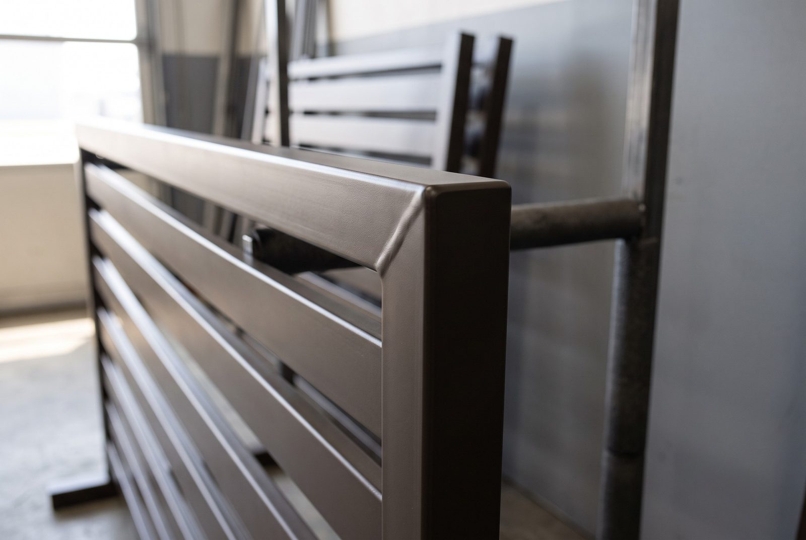 Design rendering of the corner of a dark bronze powder coated steel slat fence panel with a smooth ground weld seam