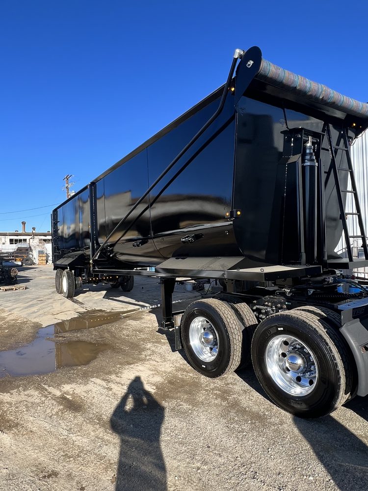 Black dump body with the tarp rolled along the front of the box